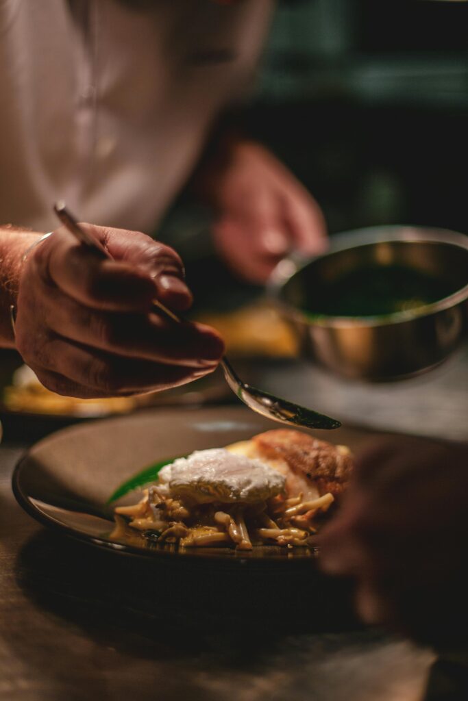 pexels-photo-2403391-2403391 Chef artistically adds sauce to a gourmet dish in a professional kitchen setting.